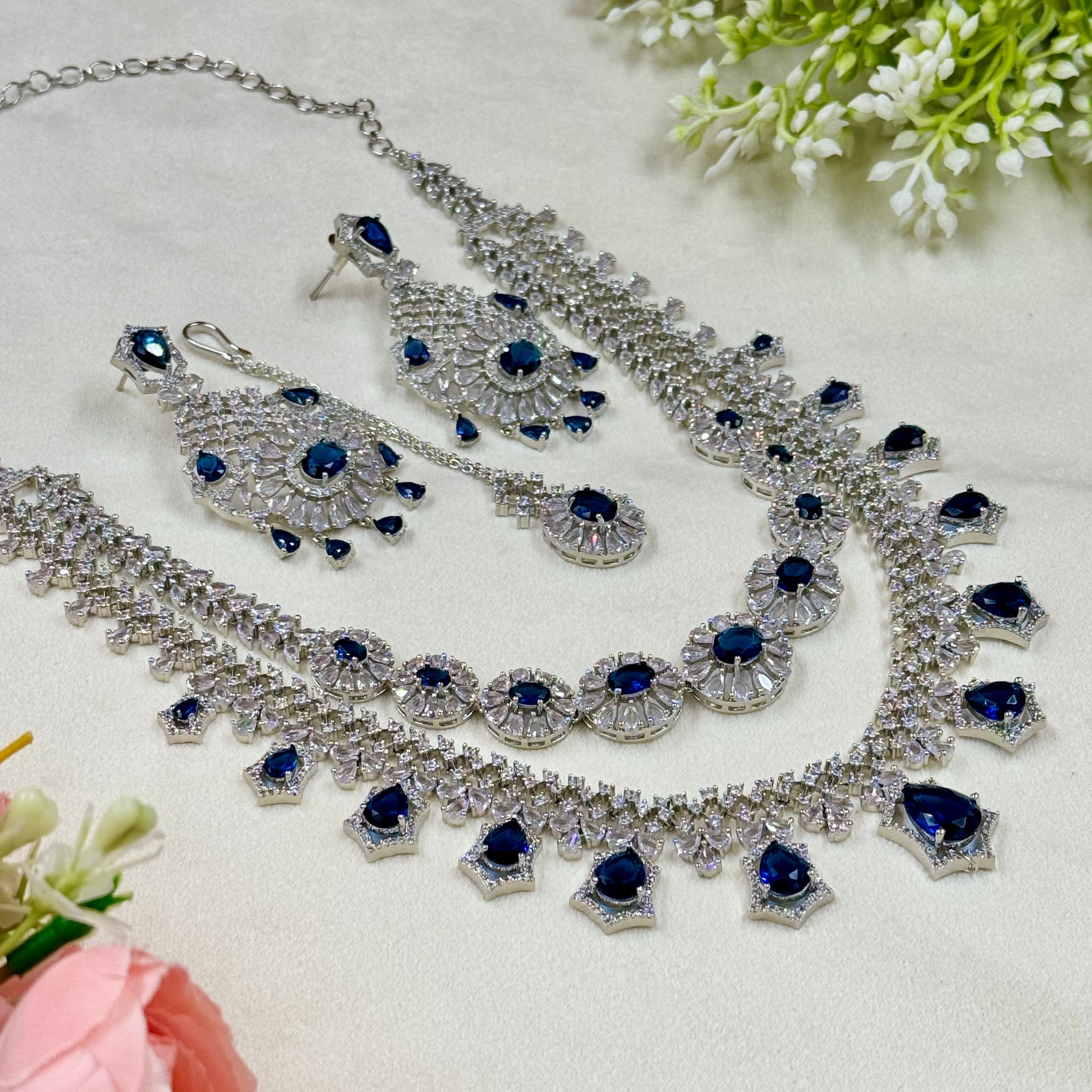 Jewelry set with necklace, earrings, and ring featuring blue stones on a light background.