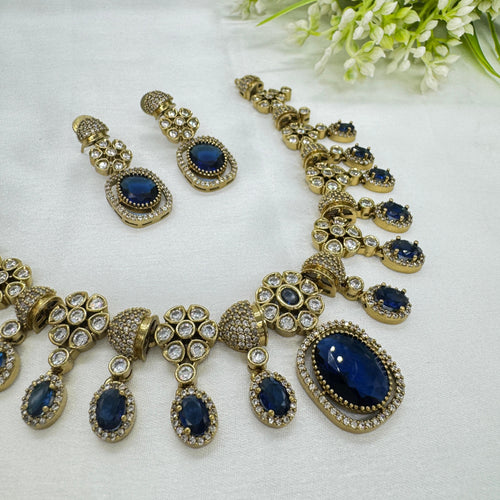 Jewelry set with necklace and earrings featuring blue stones and gold accents on a white background.