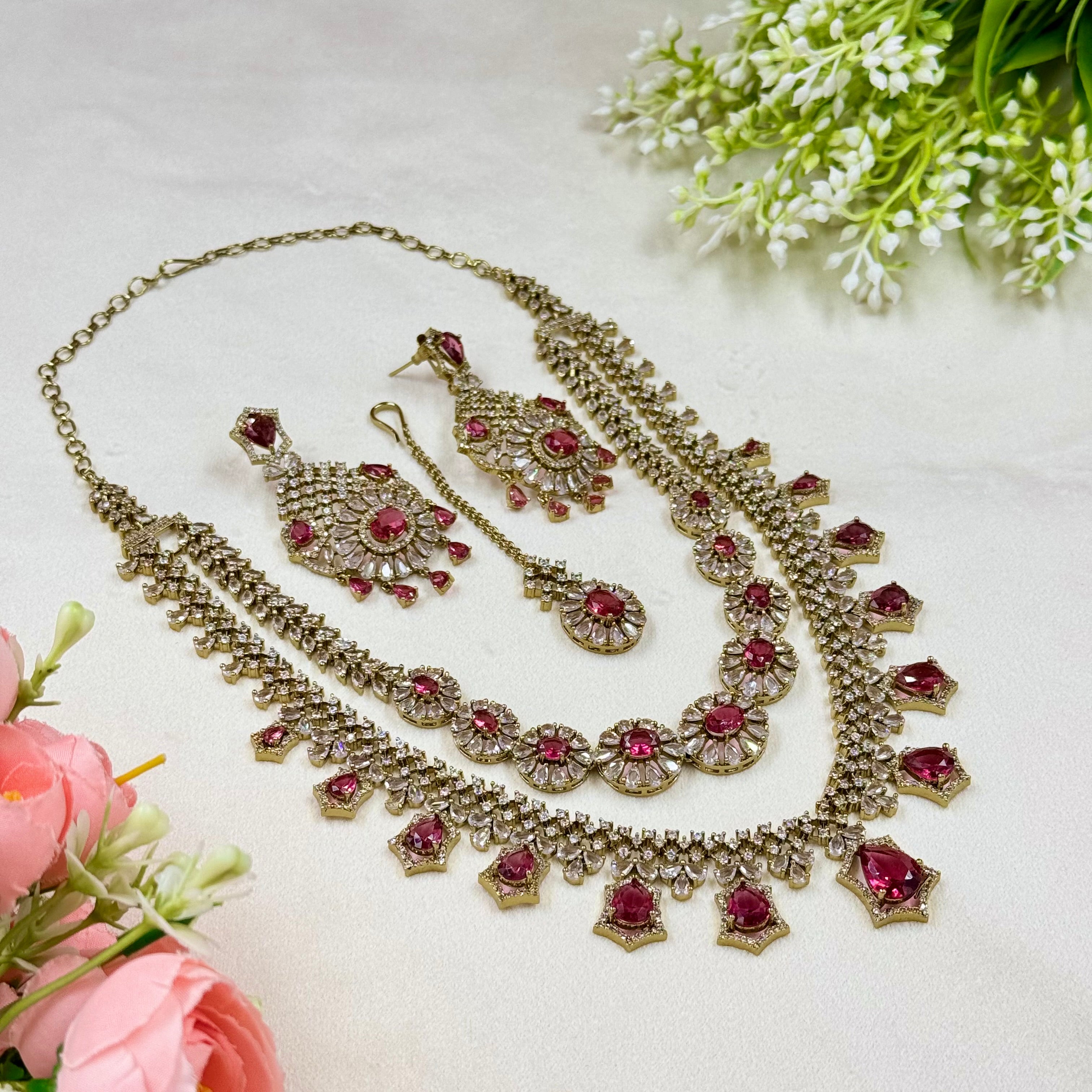 Ornate necklace set with pink stones on a light background with flowers.