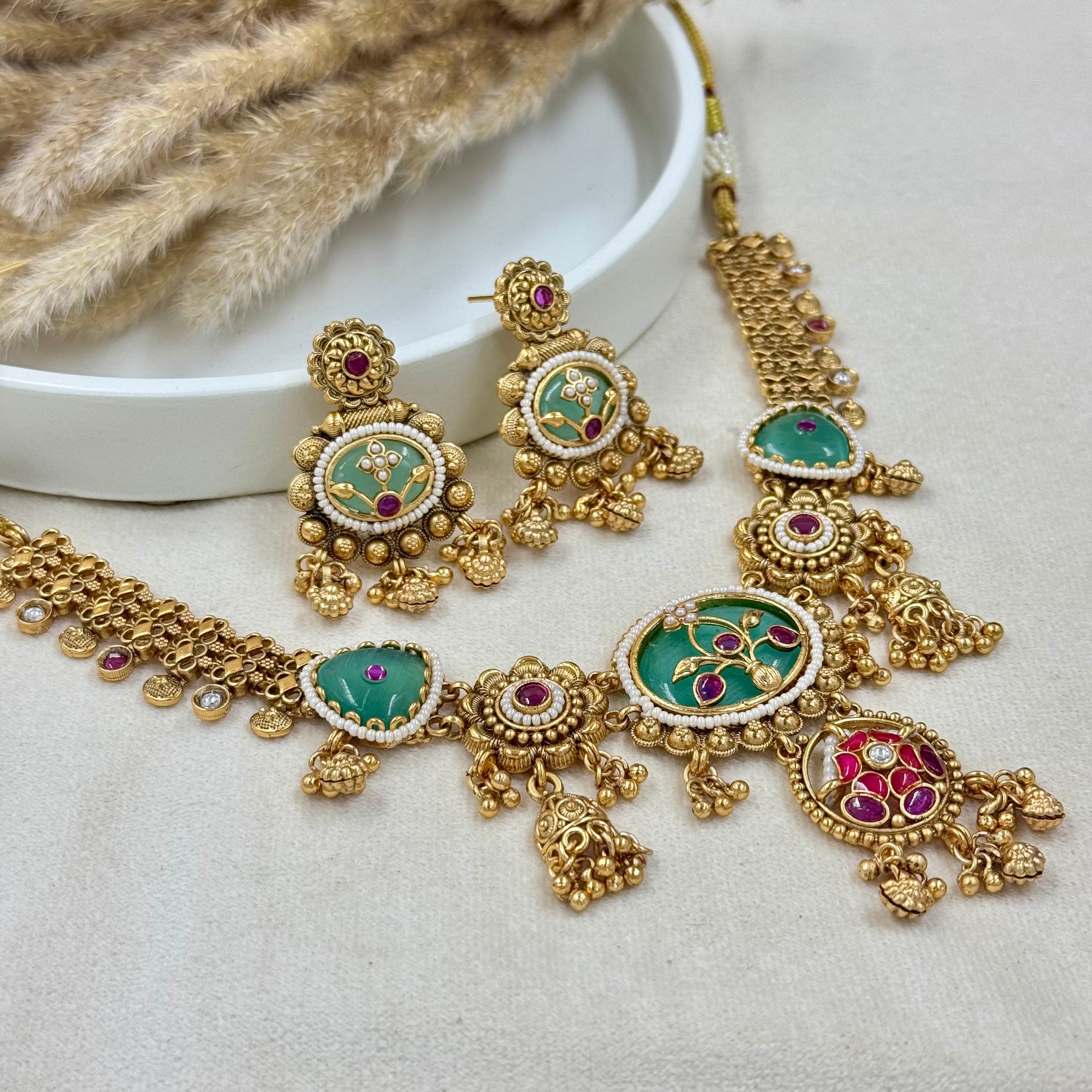 Gold necklace and earrings with green and red stones on a white surface