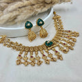 Gold necklace with green and red accents on a white surface