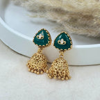 Gold and green earrings on a white surface with a fur background