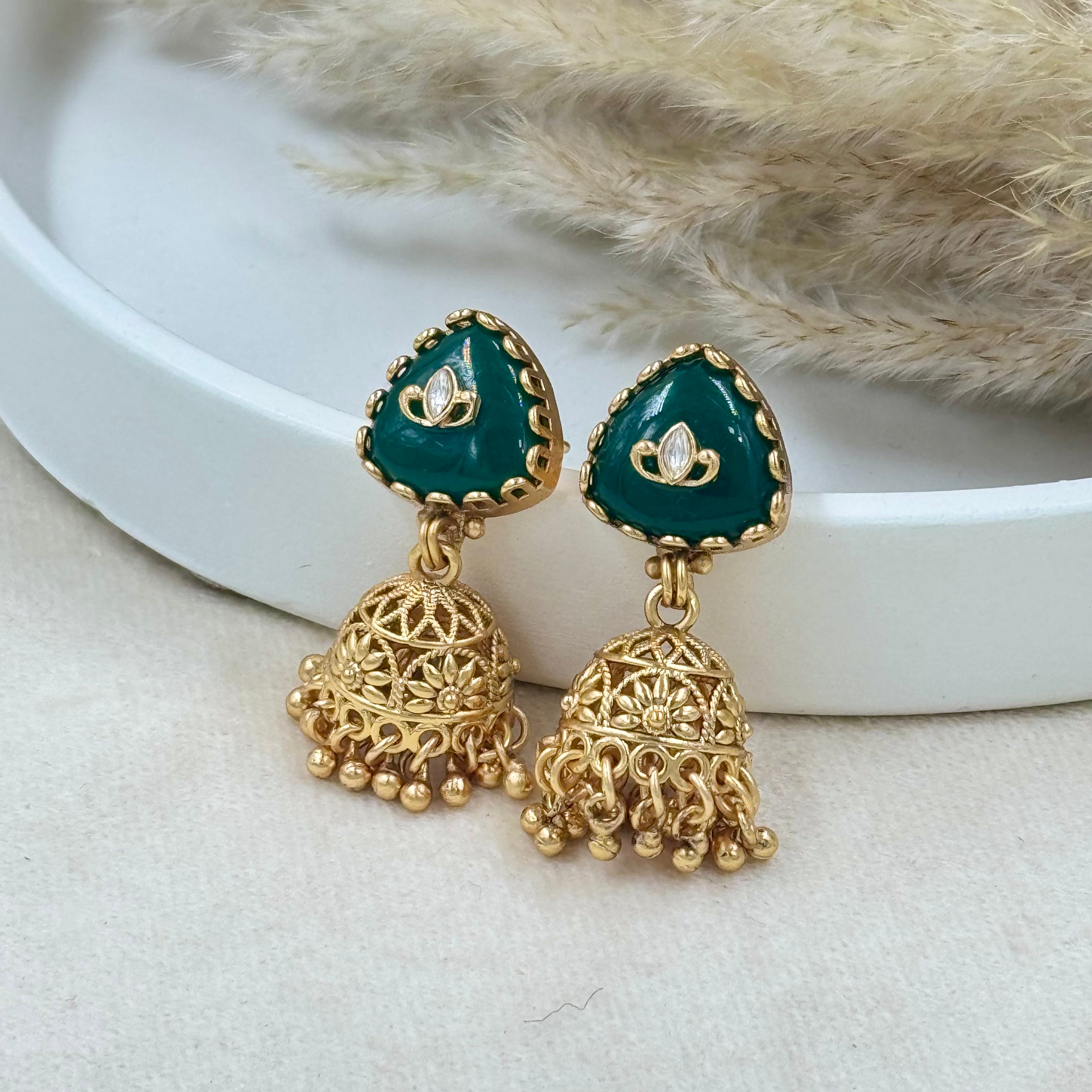 Gold and green earrings on a white surface with a fur background