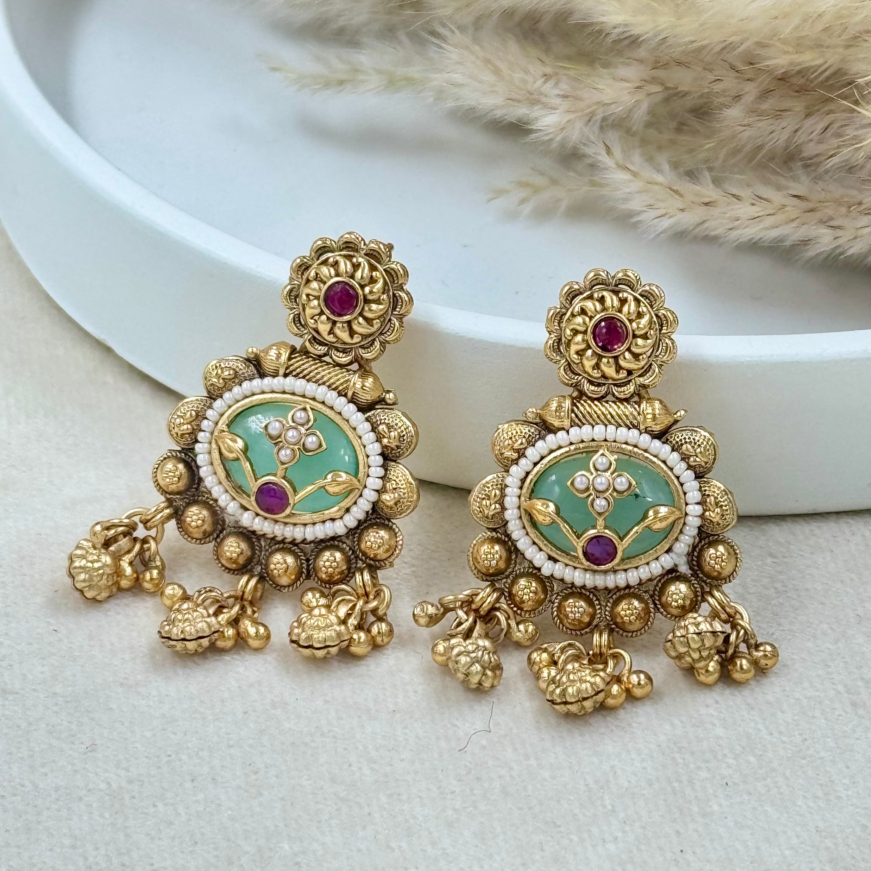 Ornate gold earrings with green and purple accents on a neutral background