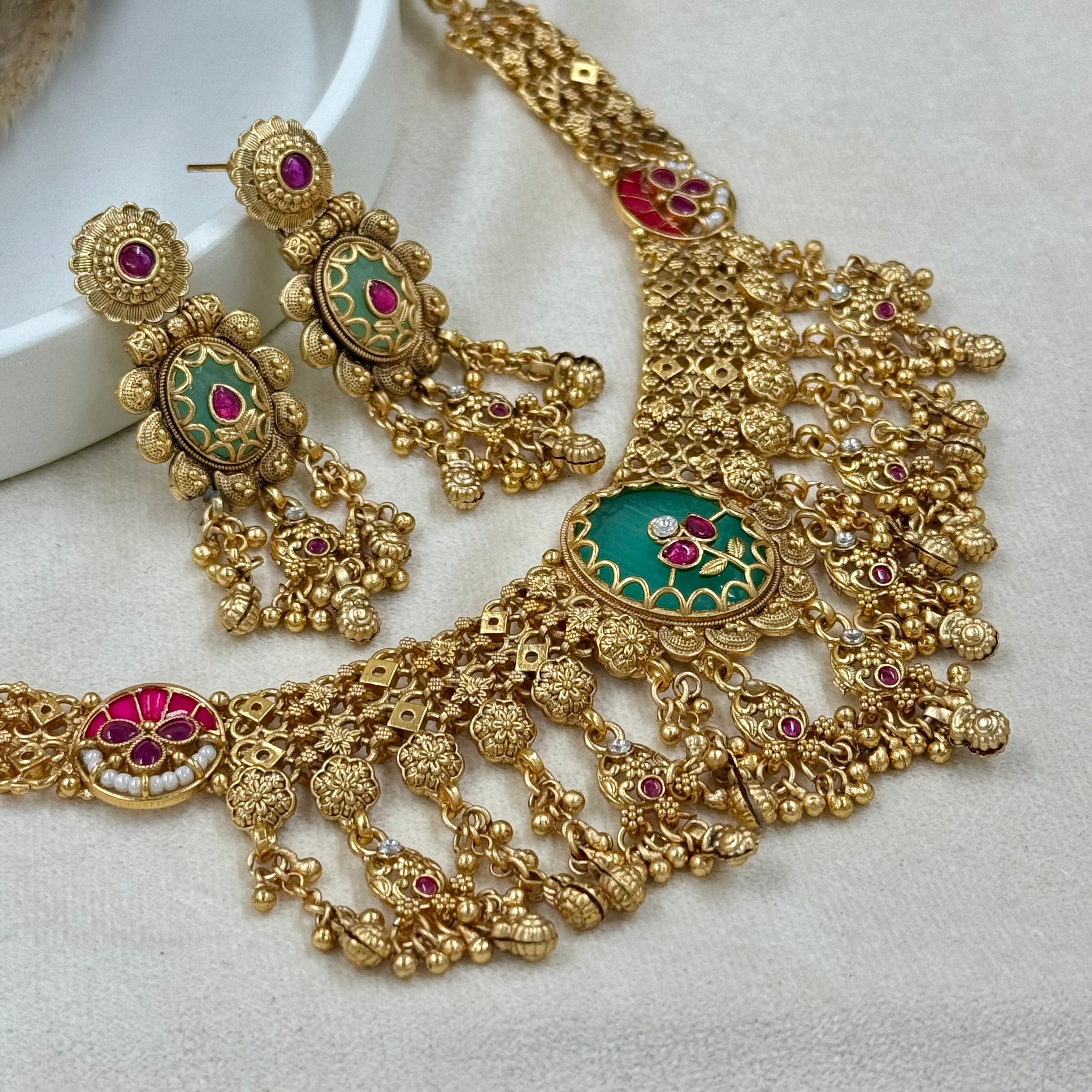 Gold necklace and earrings with green and red accents on a white background