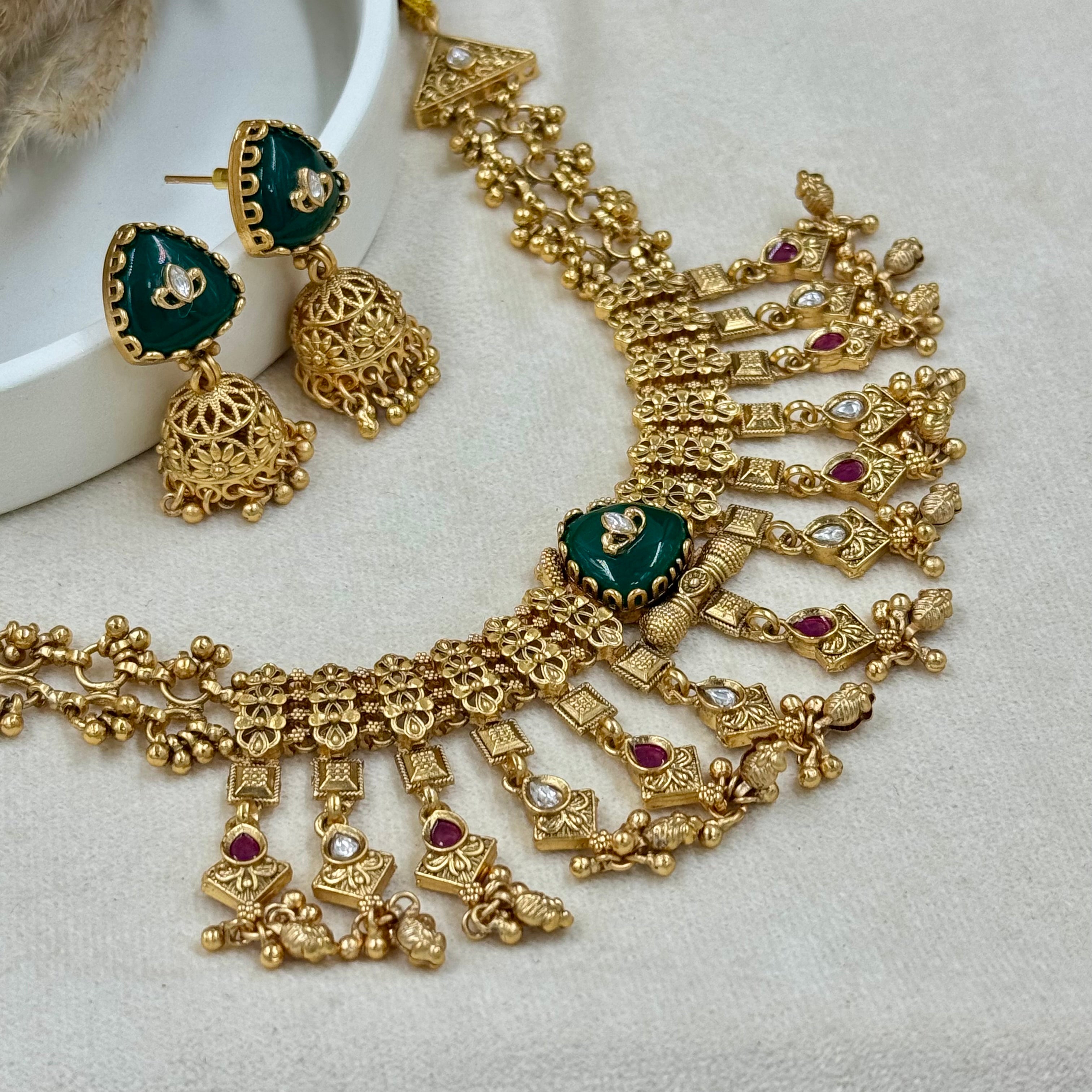 Gold necklace with green and red gemstones on a light gray background