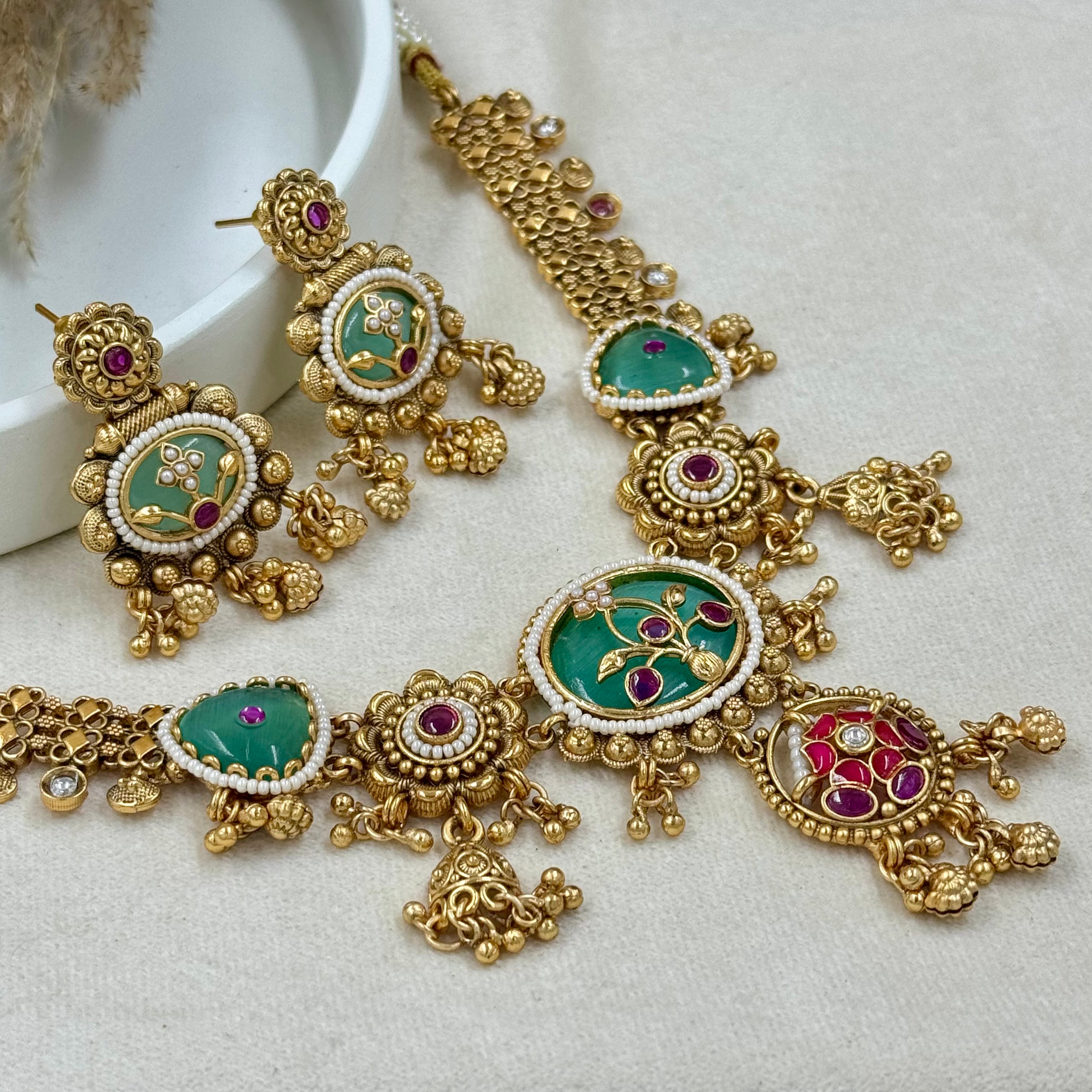Ornate gold necklace with green and red gemstones on a light background