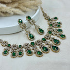 Green gemstone necklace and earrings on a white surface with dried plants in the background