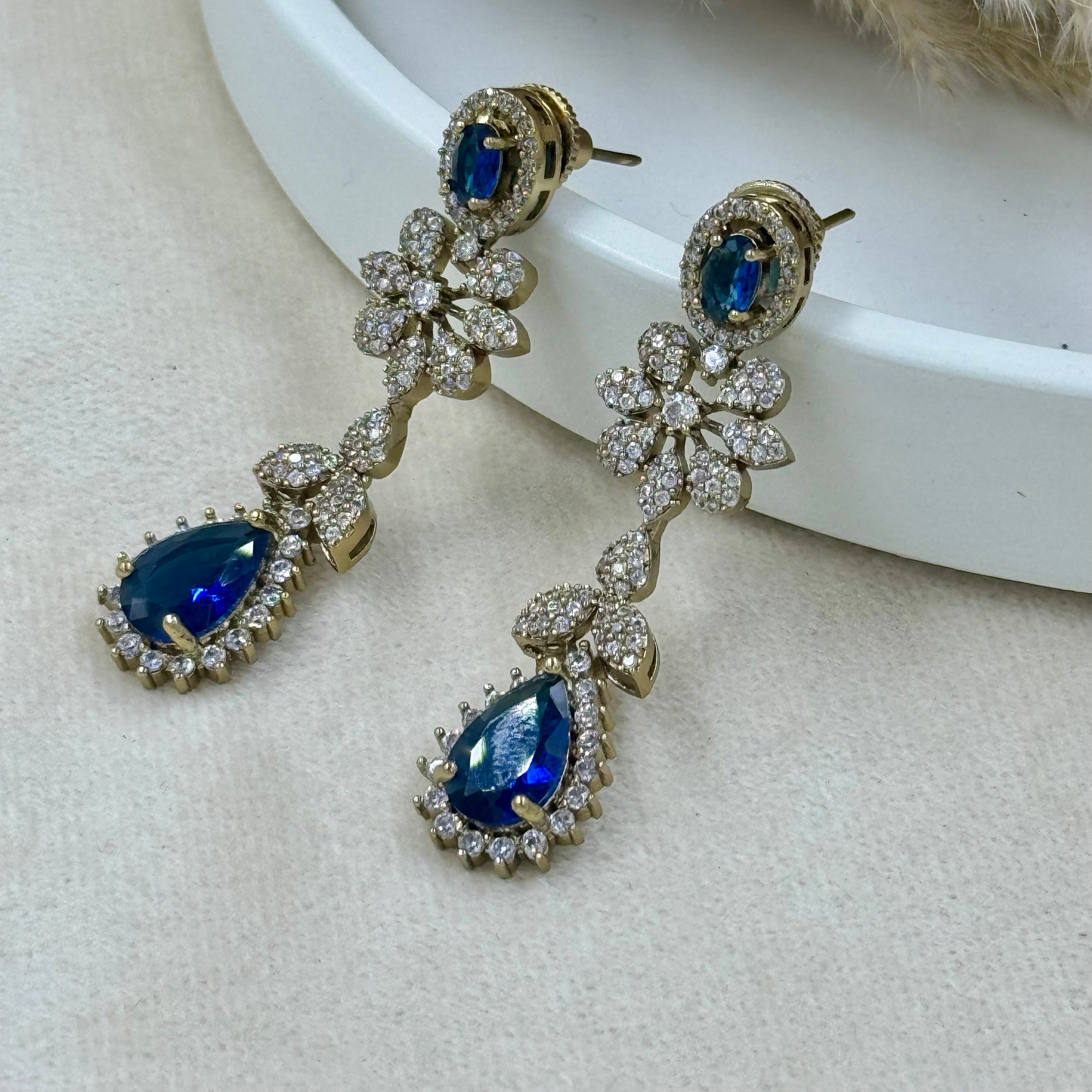 Pair of gold earrings with blue gemstones on a light background