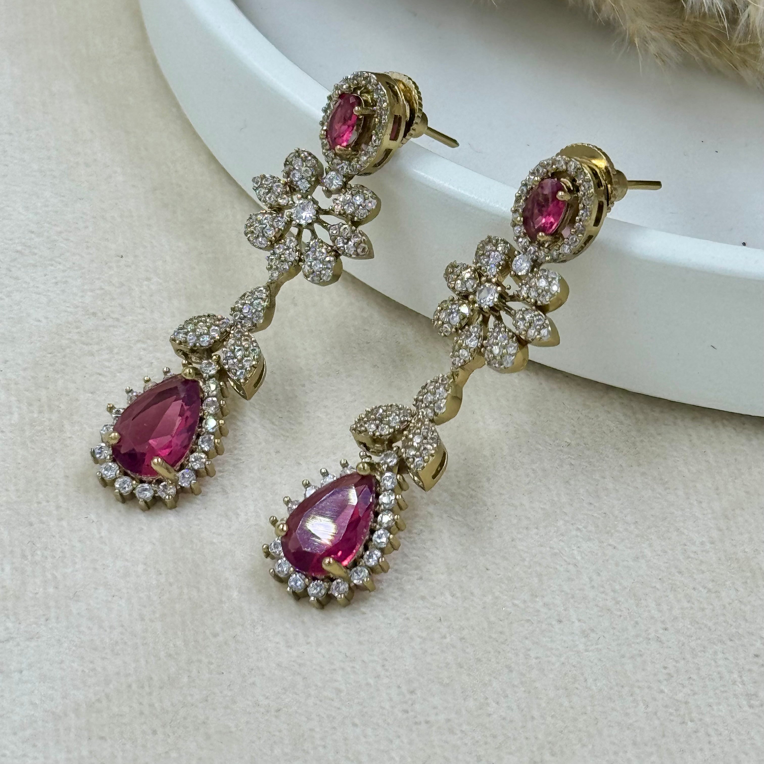 Gold earrings with pink gemstones on a beige surface