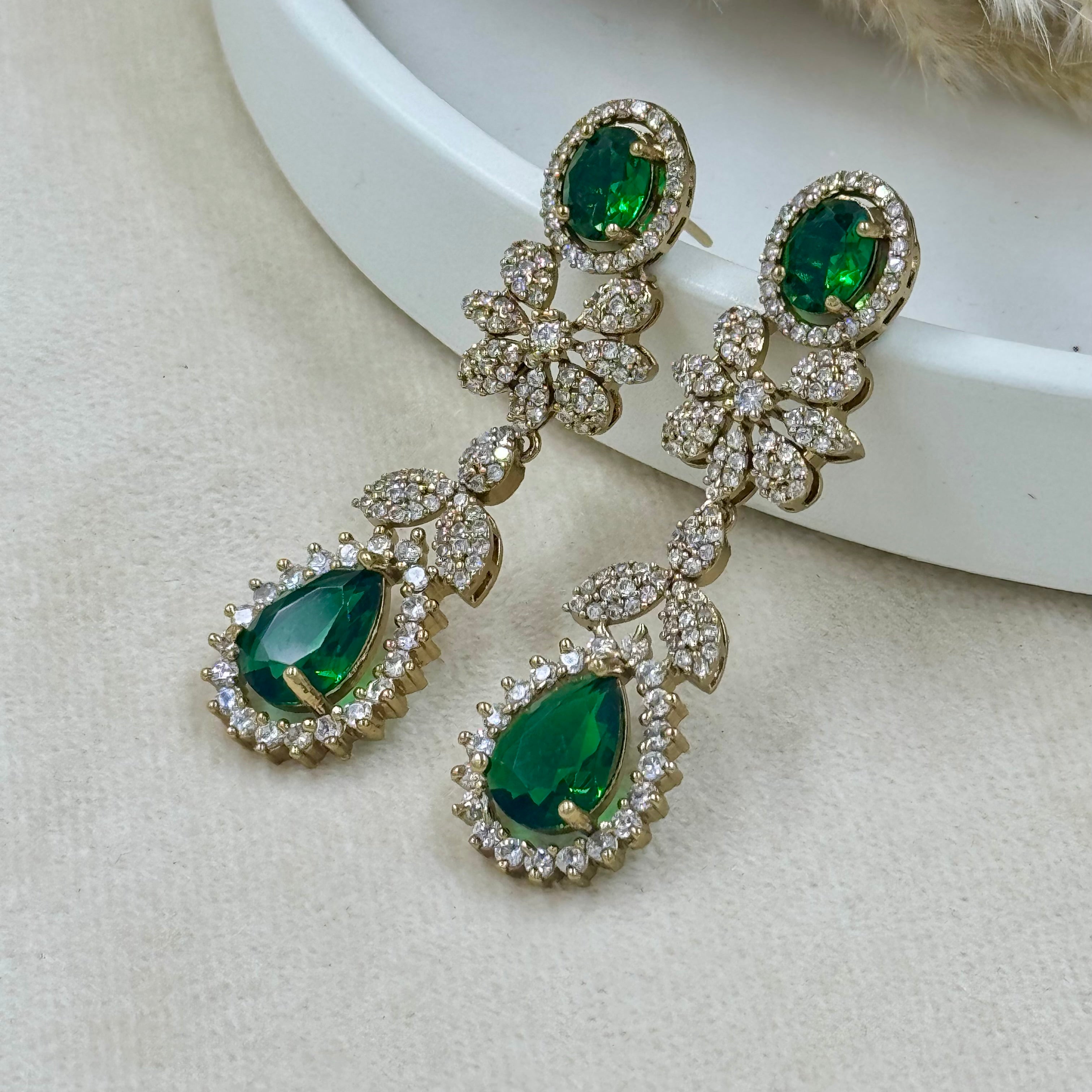 Pair of earrings with green gemstones and gold accents on a light background