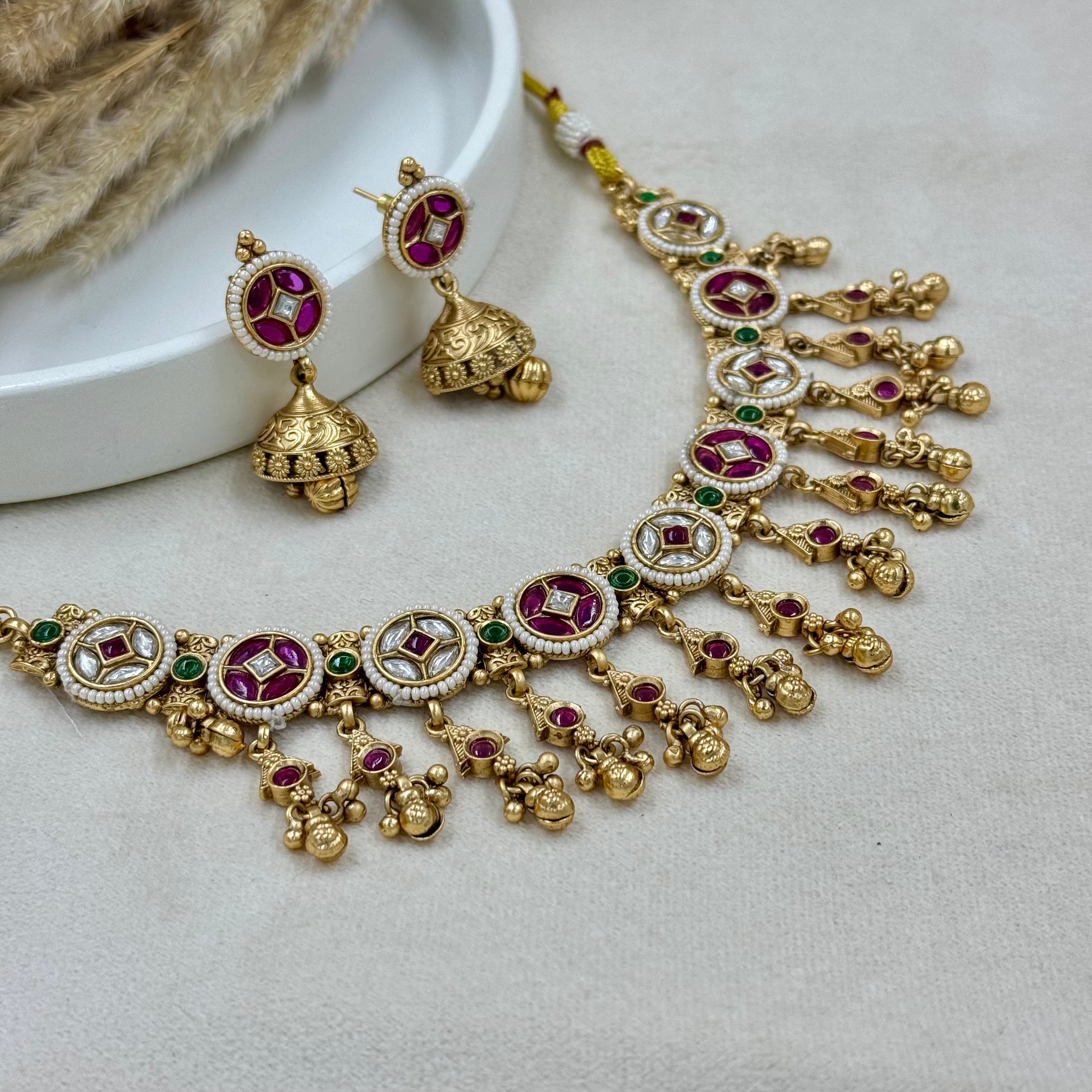 Gold necklace with red and green gemstones on a light gray surface