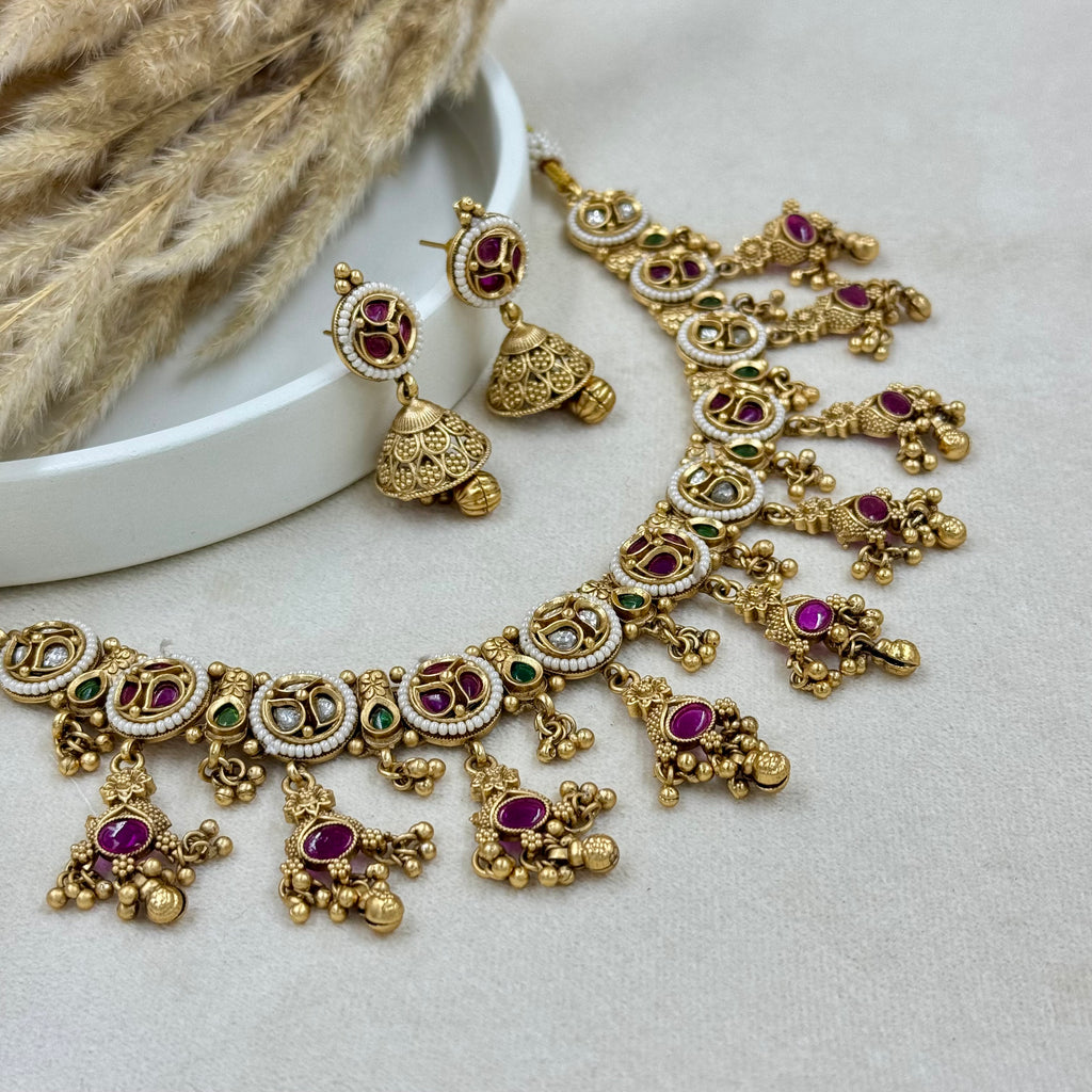 Gold necklace with red and green gemstones on a light gray surface