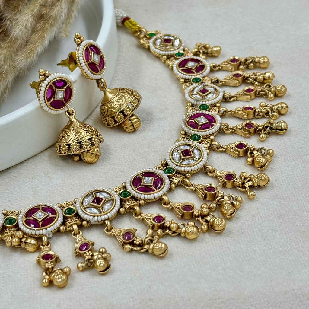 Ornate gold necklace with red and green gemstones on a light background