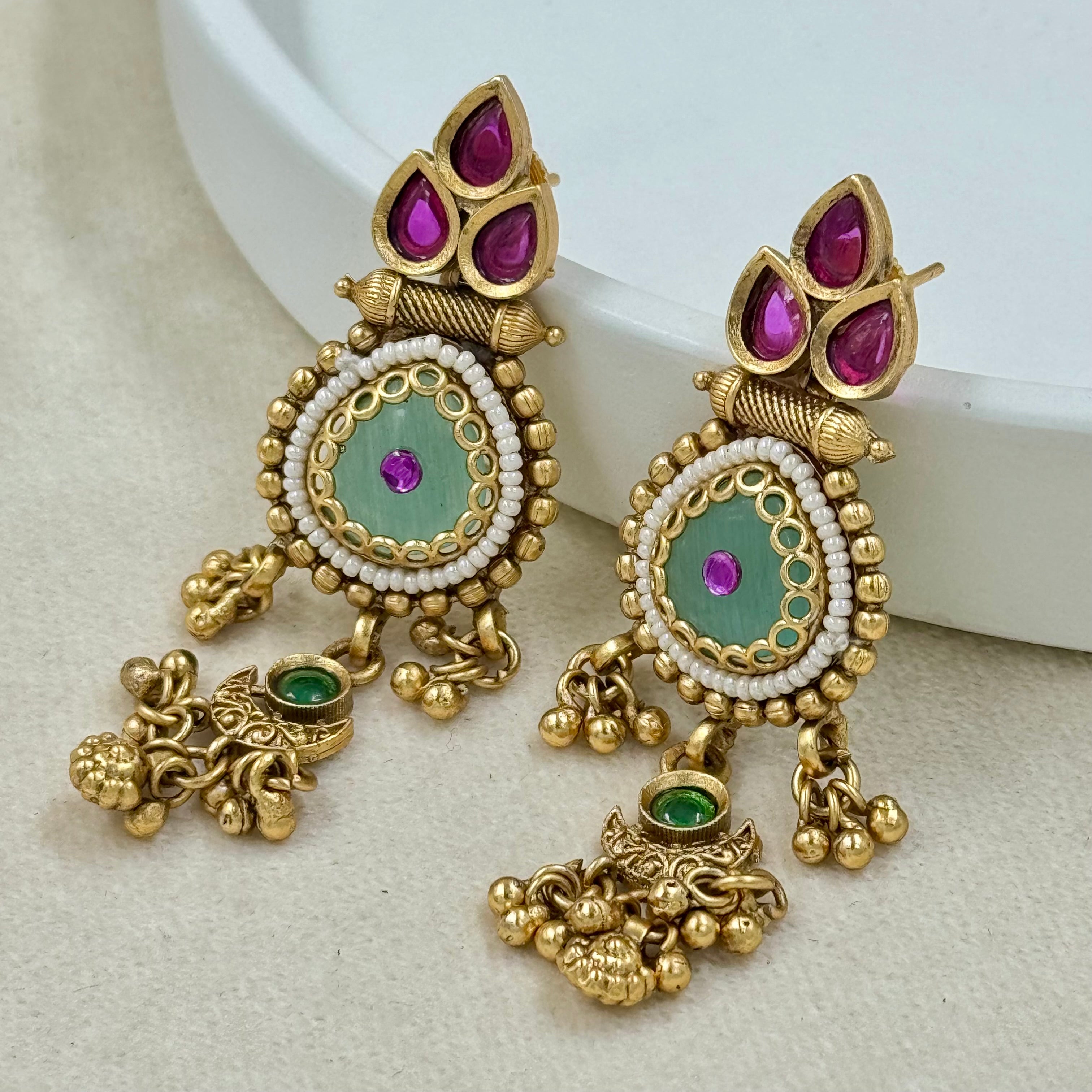 Ornate gold earrings with gemstones on a light background