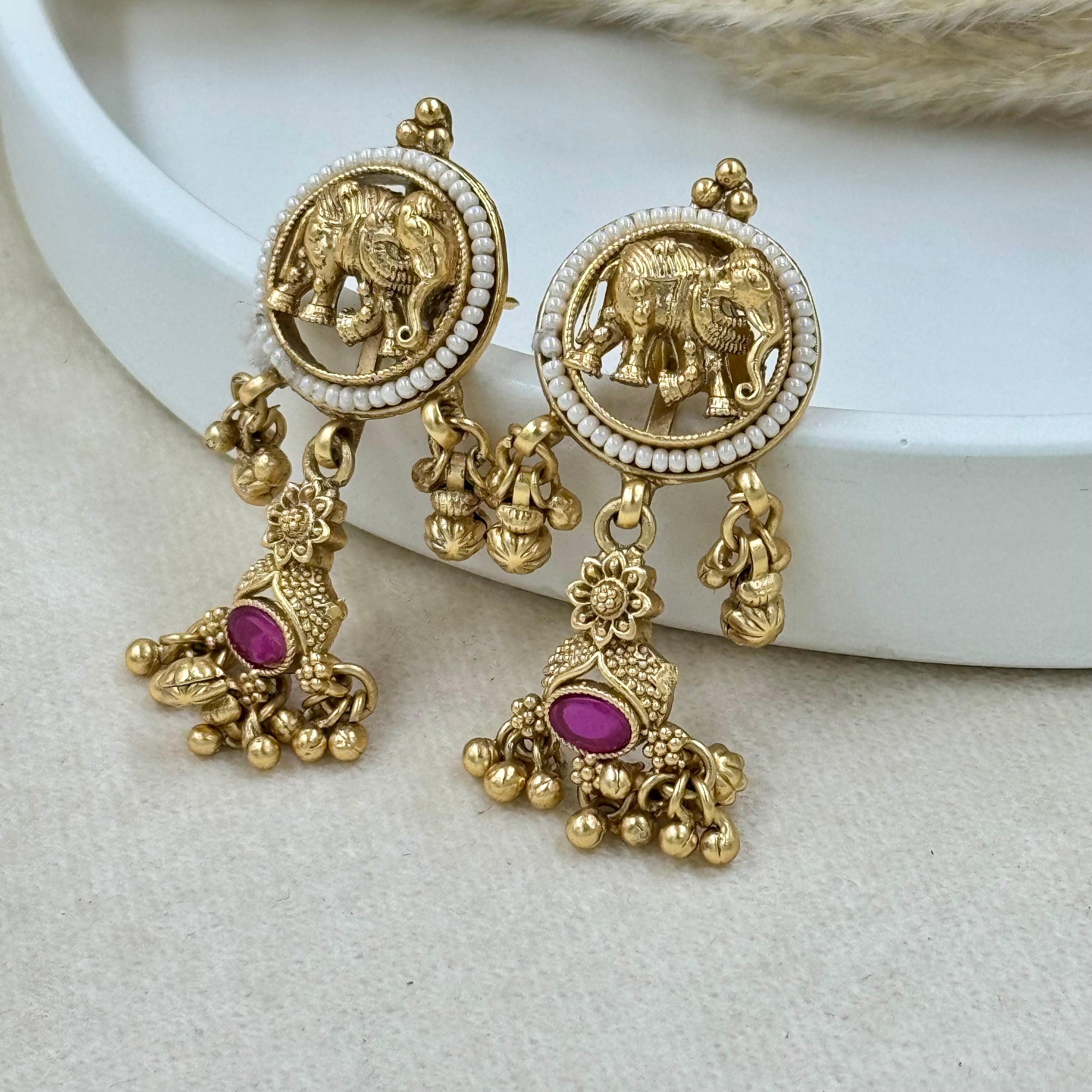 Gold earrings with elephant design and pink stones on a white surface