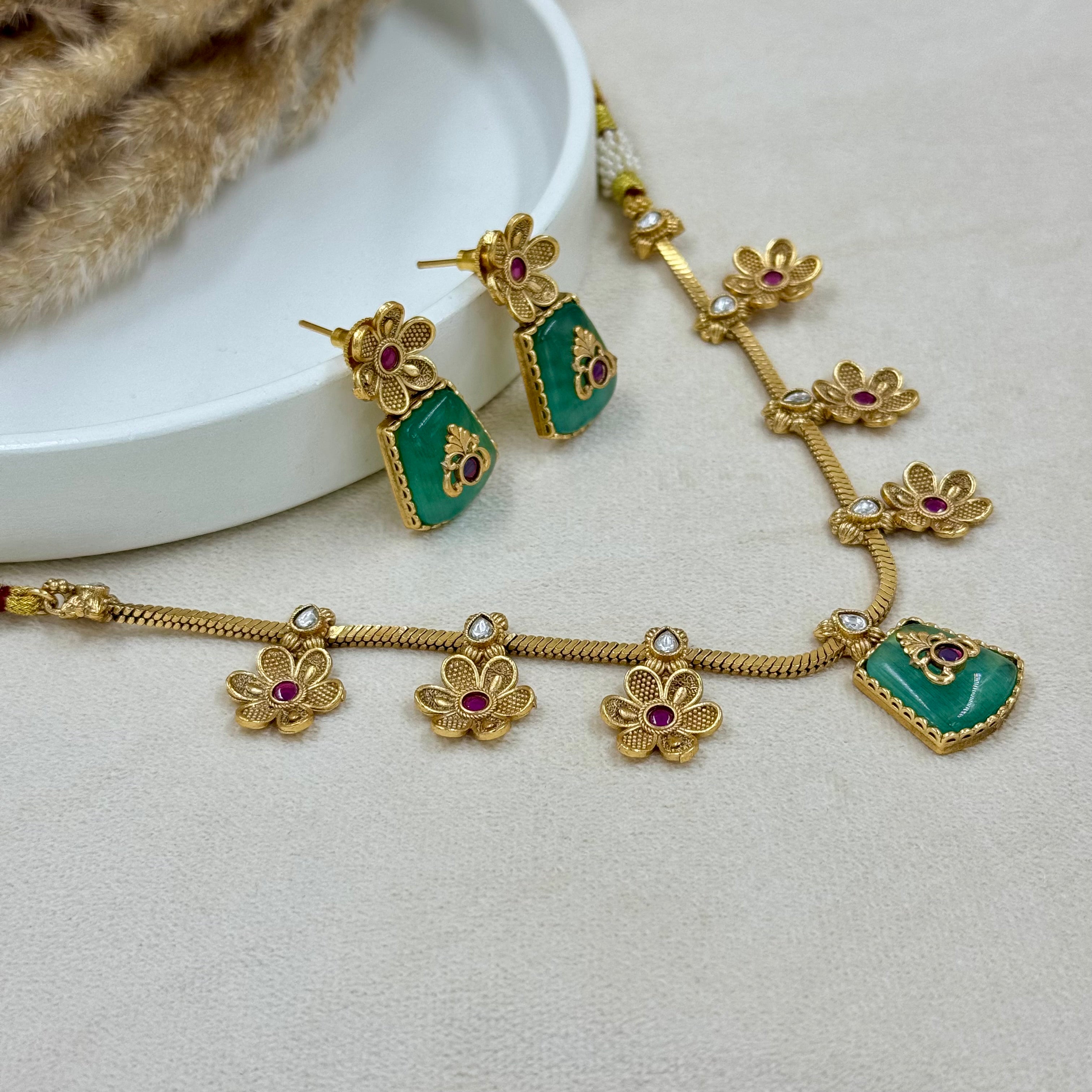 Gold necklace with green pendants and red gemstones on a light gray surface.