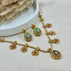 Gold necklace with green and red gemstones on a light gray surface