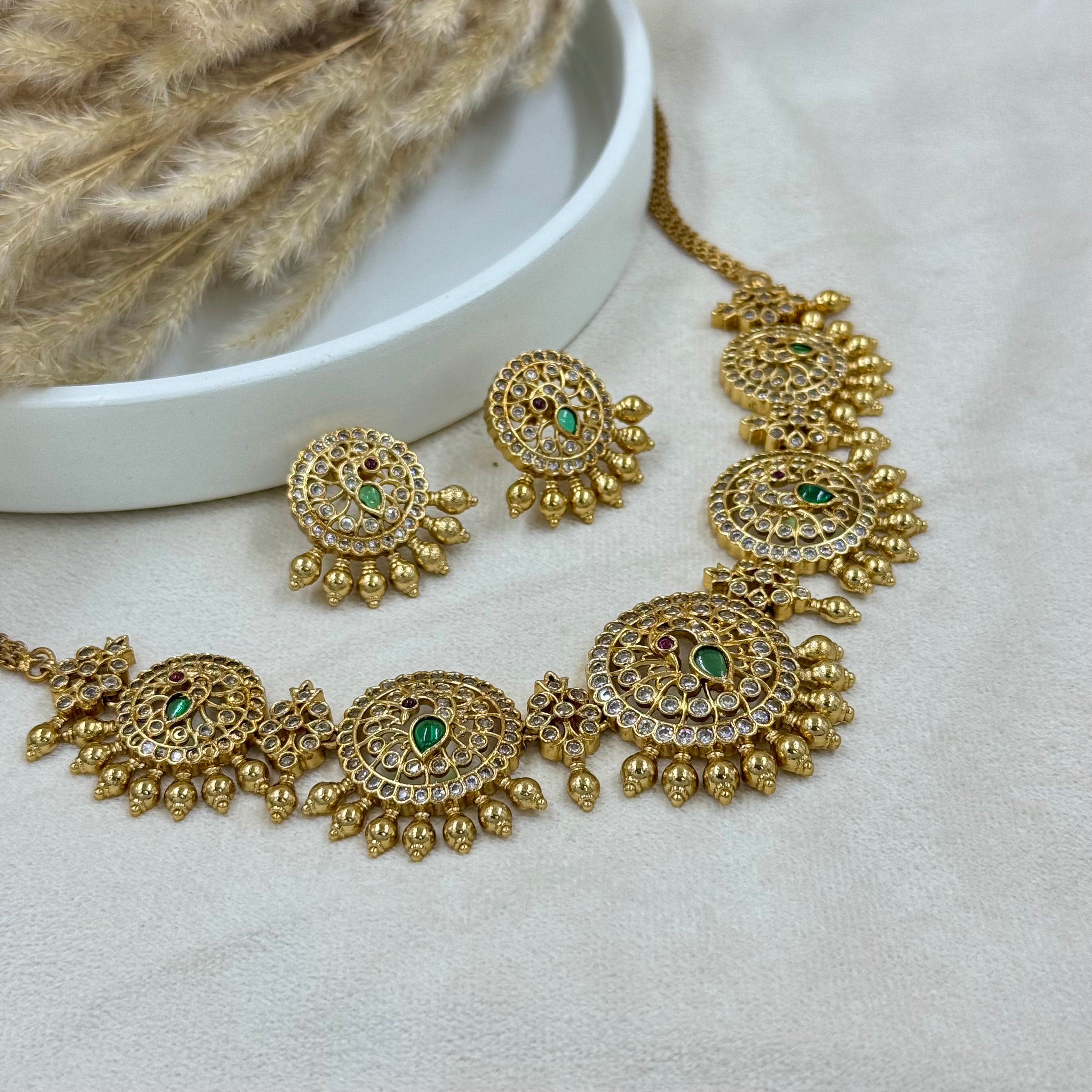 Gold necklace and earrings with green stones on a light background