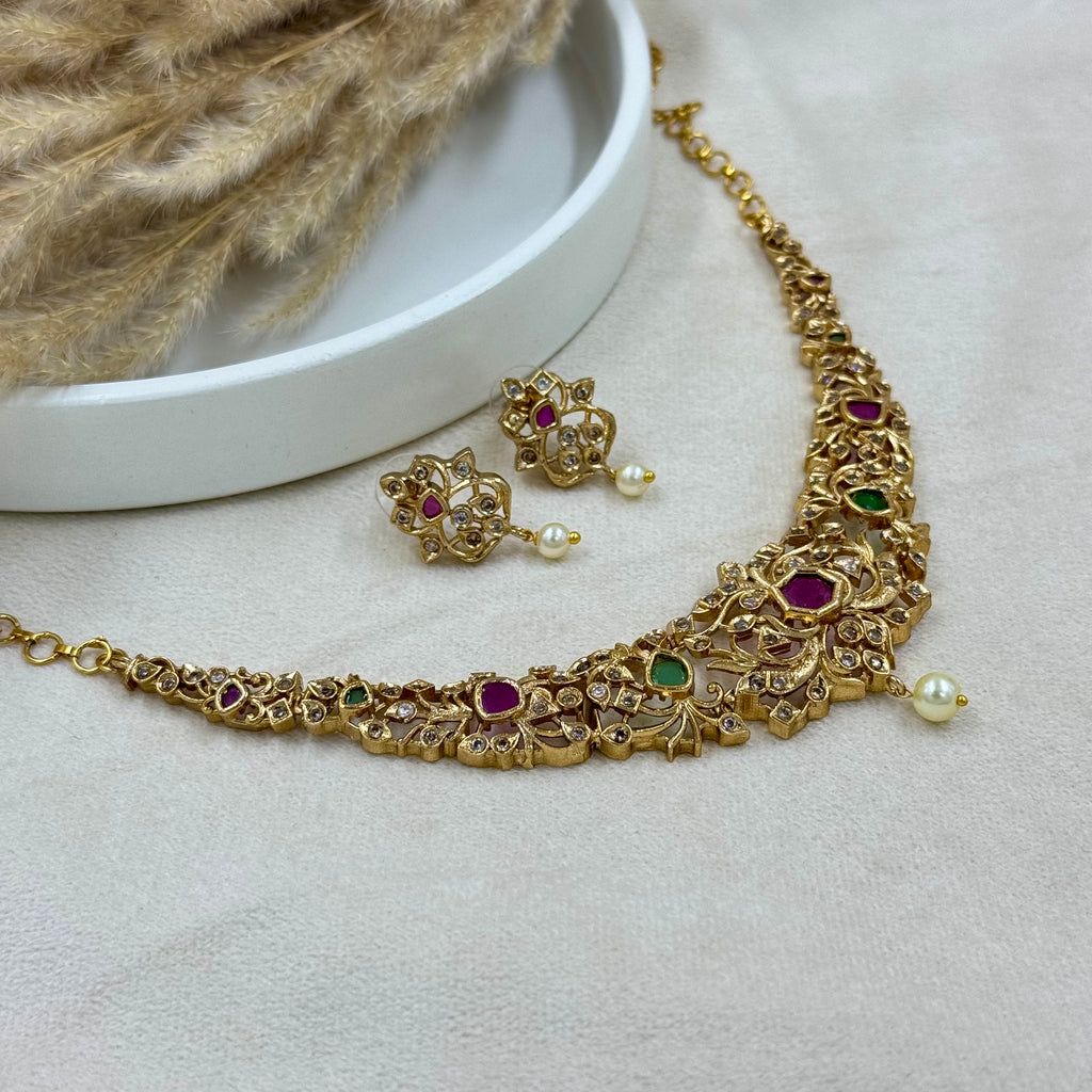 Gold necklace with gemstones and earrings on a light gray surface