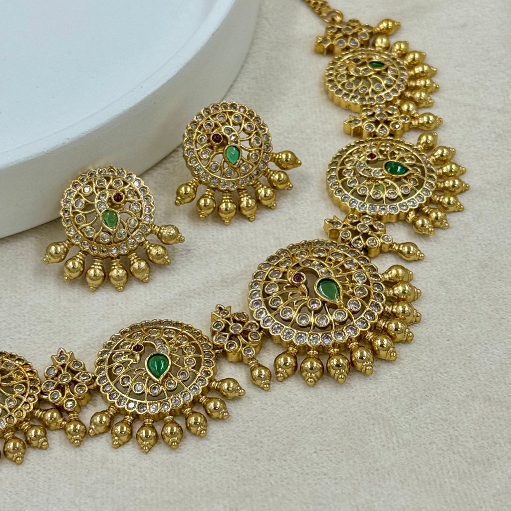 Gold necklace with green gemstones on a light gray background