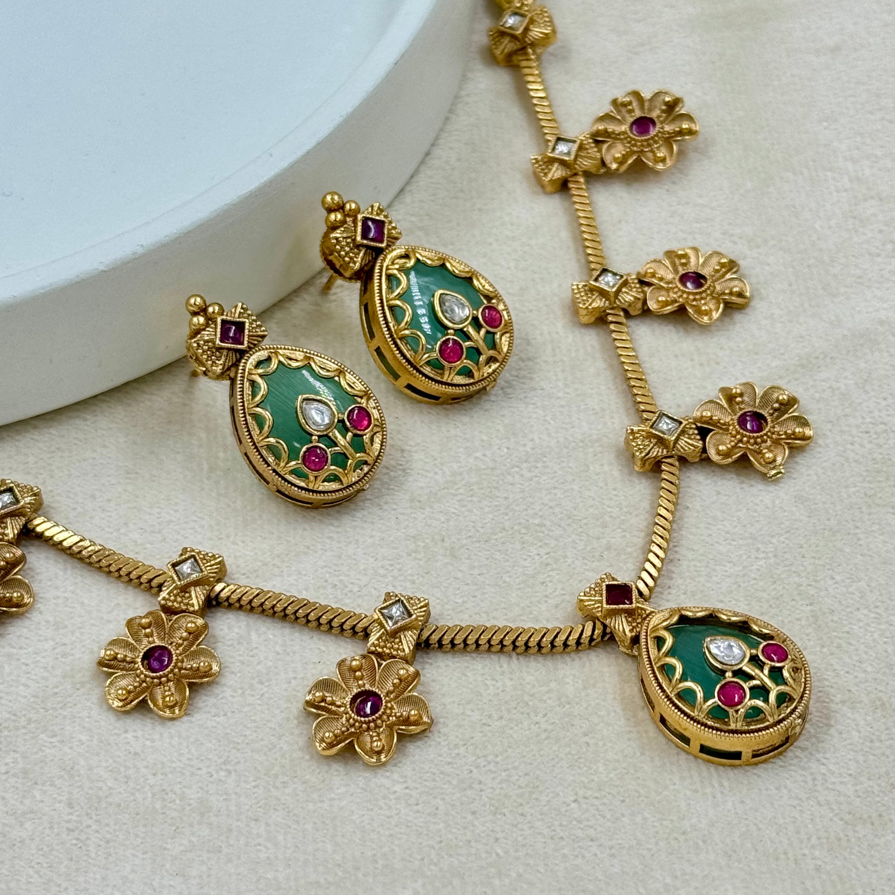 Gold necklace with green and red gemstones on a light background