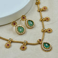 Gold necklace with green gemstones and red stones on a beige background