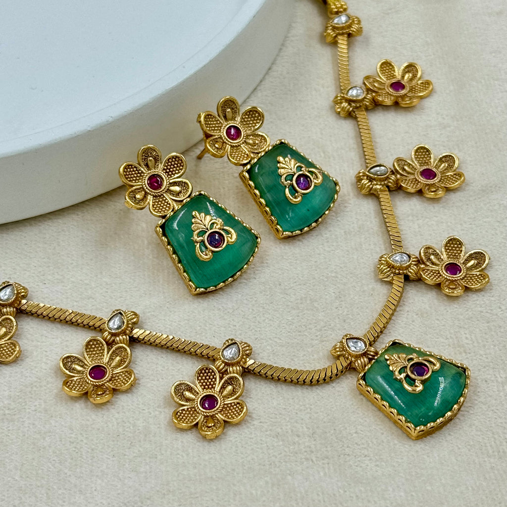 Gold necklace with green gemstones and red stones on a beige background
