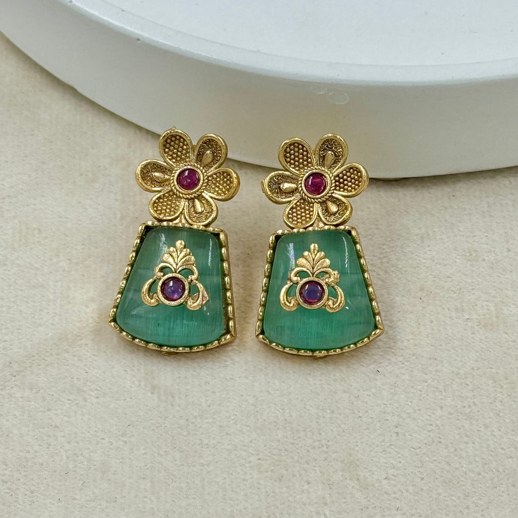 Gold and green earrings with purple gemstones on a beige surface