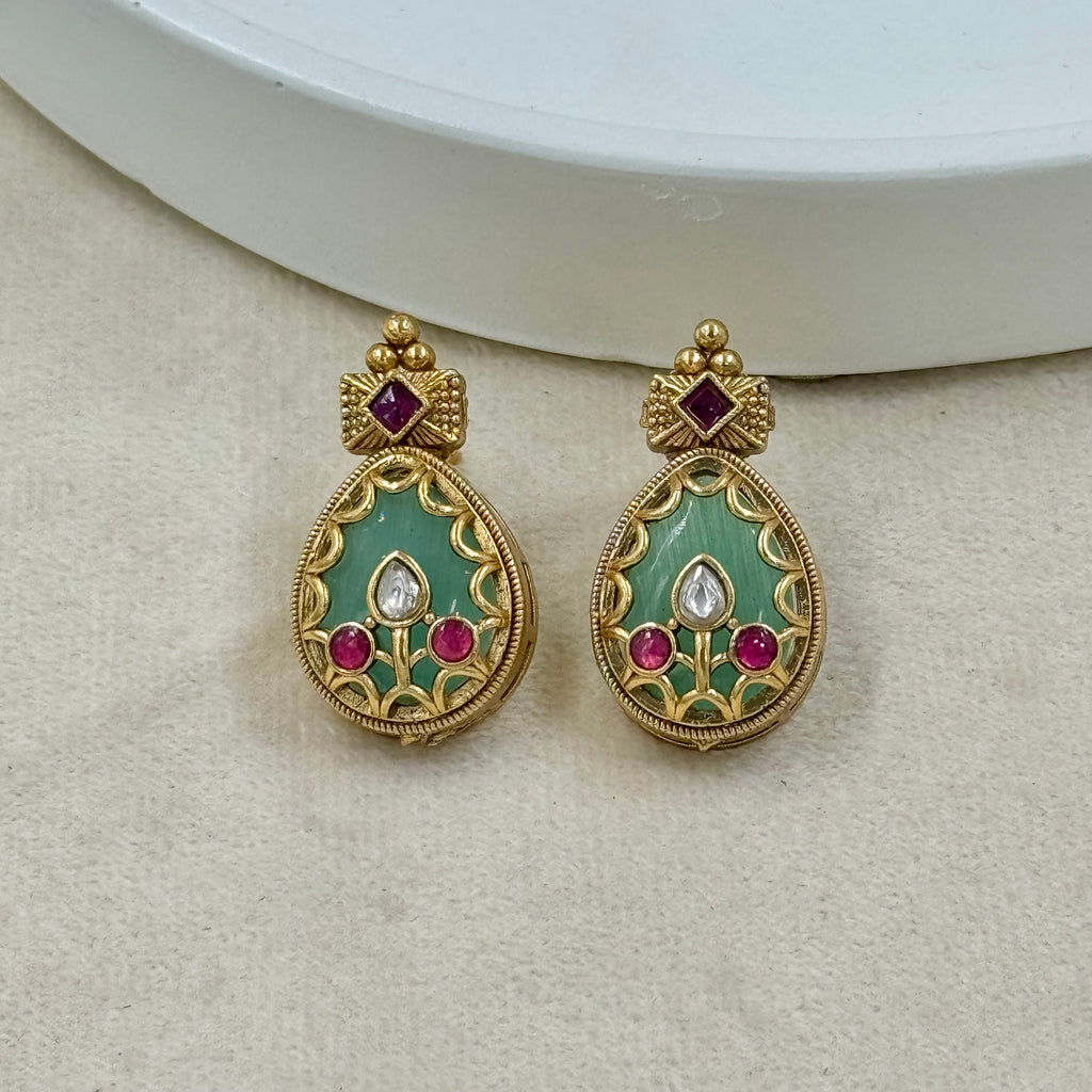Pair of gold earrings with green and red gemstones on a beige surface