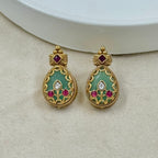 Pair of gold earrings with green and red gemstones on a beige surface