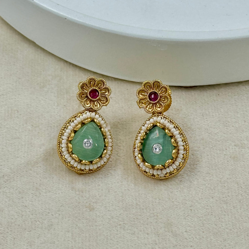 Gold earrings with green gemstones on a beige surface