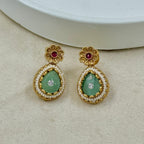 Gold earrings with green gemstones on a beige surface