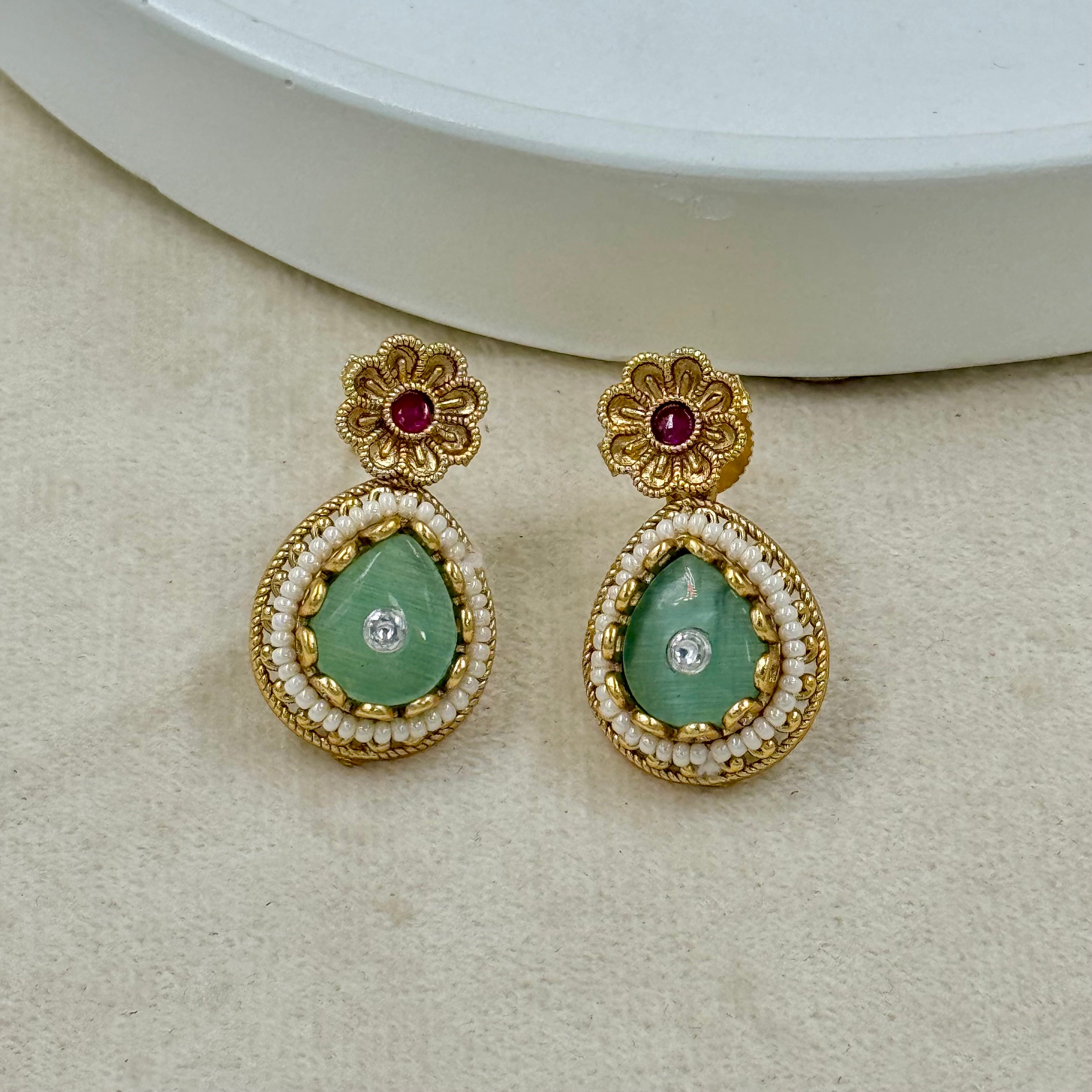 Gold earrings with green gemstones on a beige surface