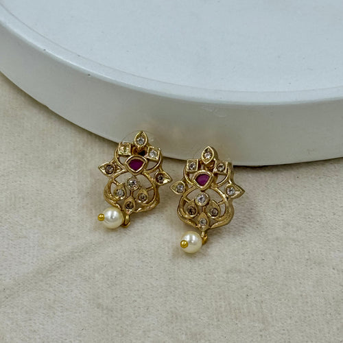 Gold earrings with red gemstones and pearls on a beige surface