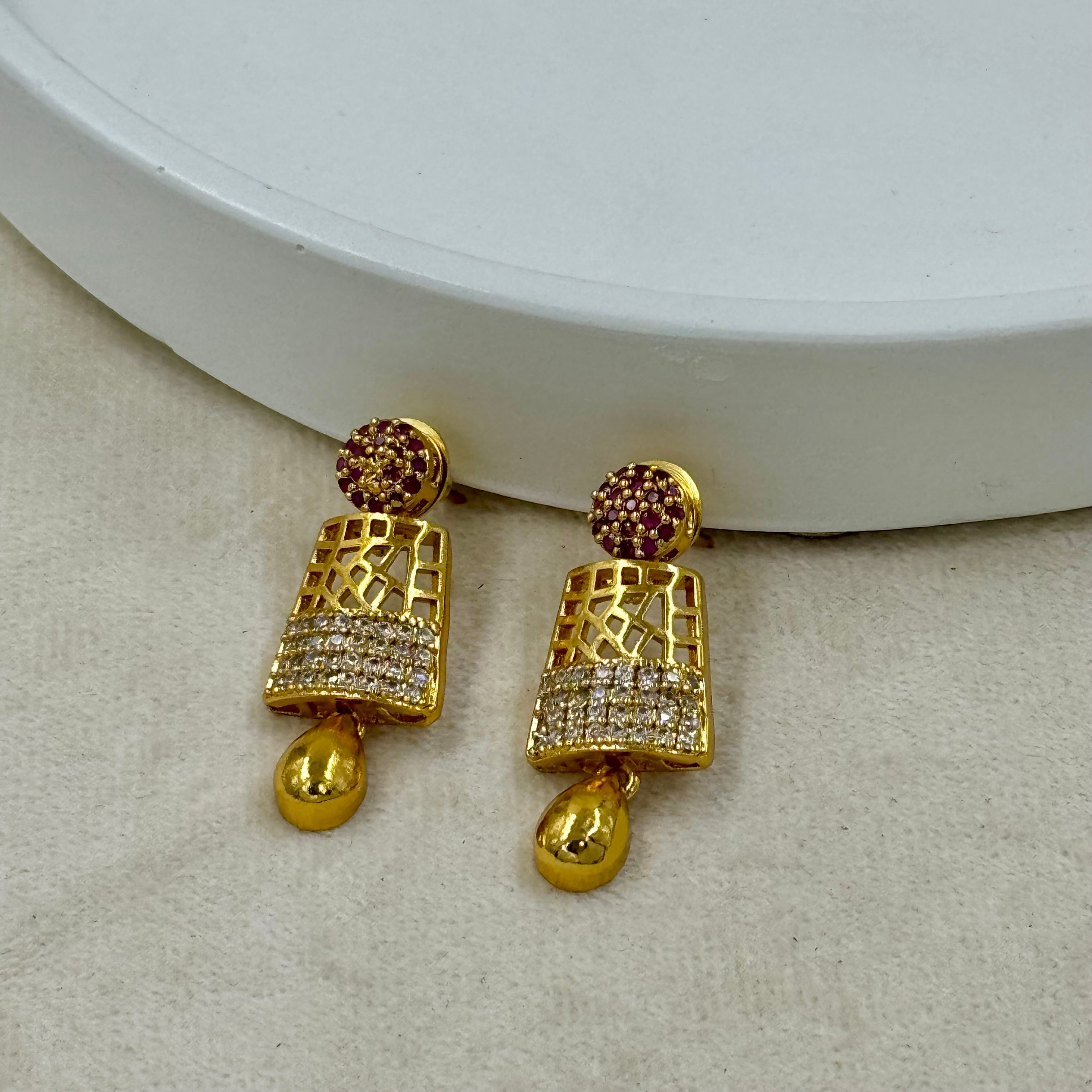 Gold earrings with intricate designs on a beige surface