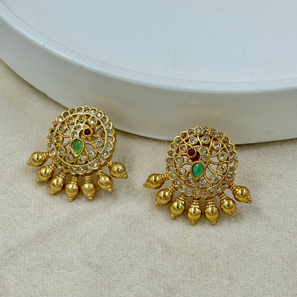 Pair of gold earrings with green and red stones on a beige surface.