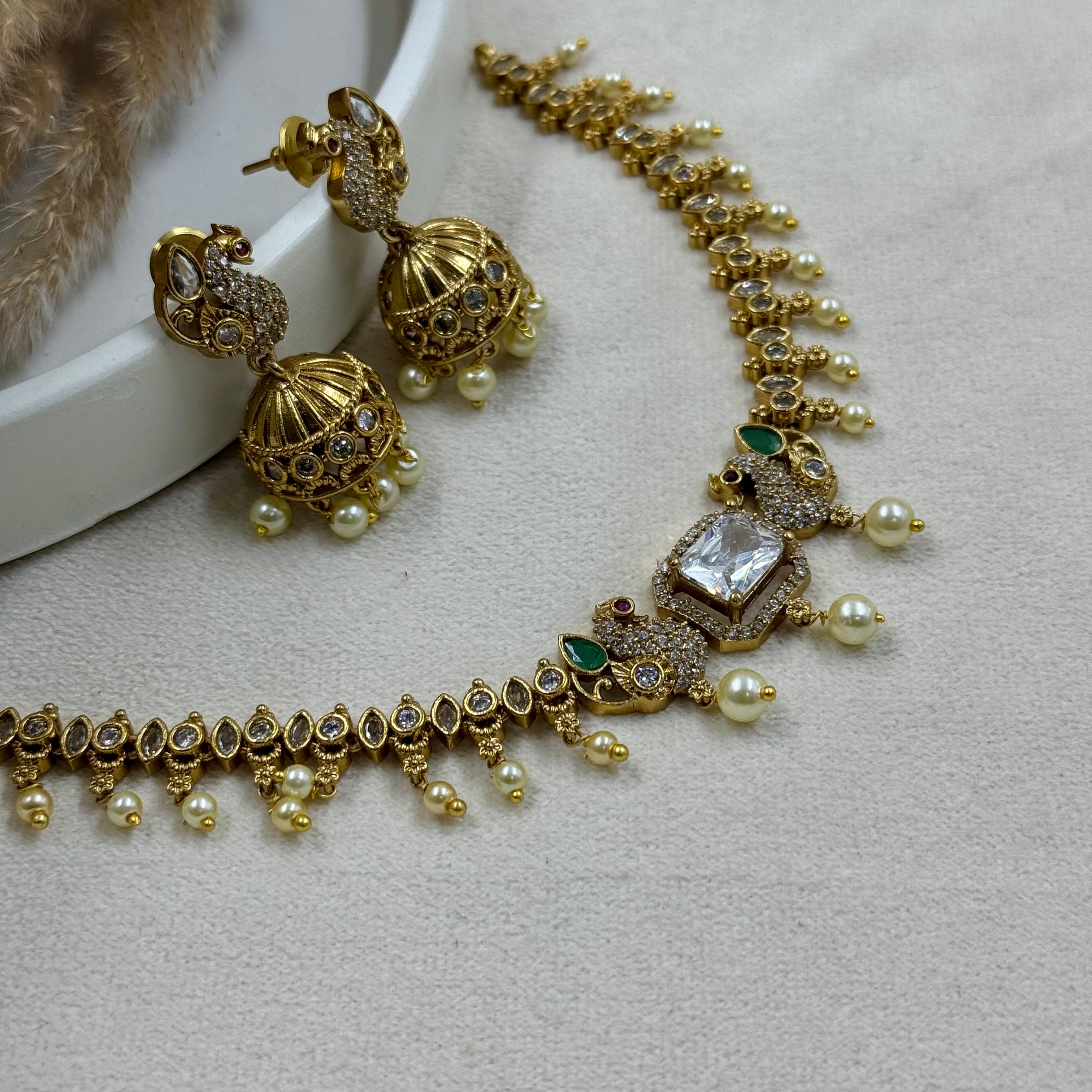 Gold necklace and earrings with pearls and gemstones on a light gray surface.