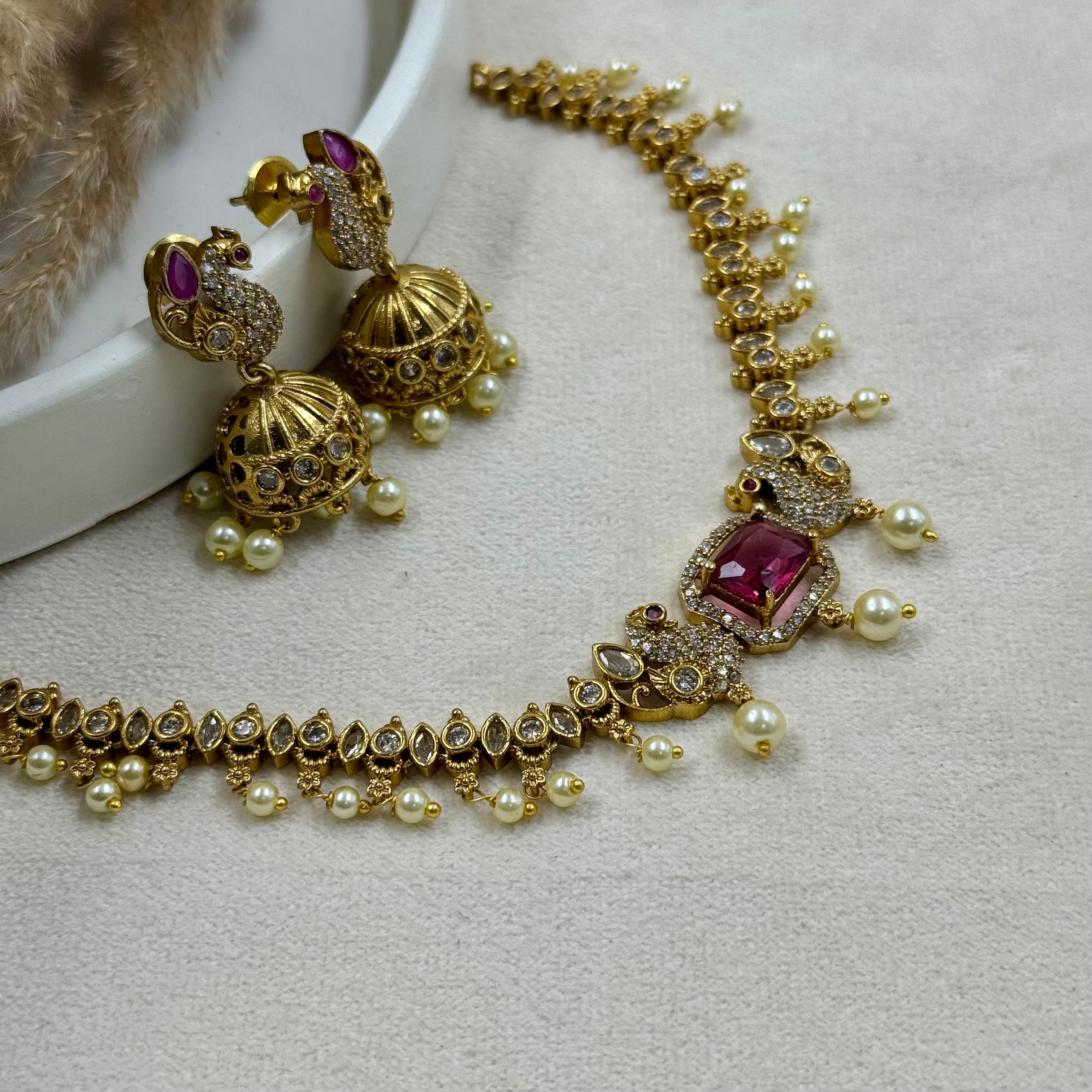 Gold necklace with red gemstones and pearl accents on a light gray surface.