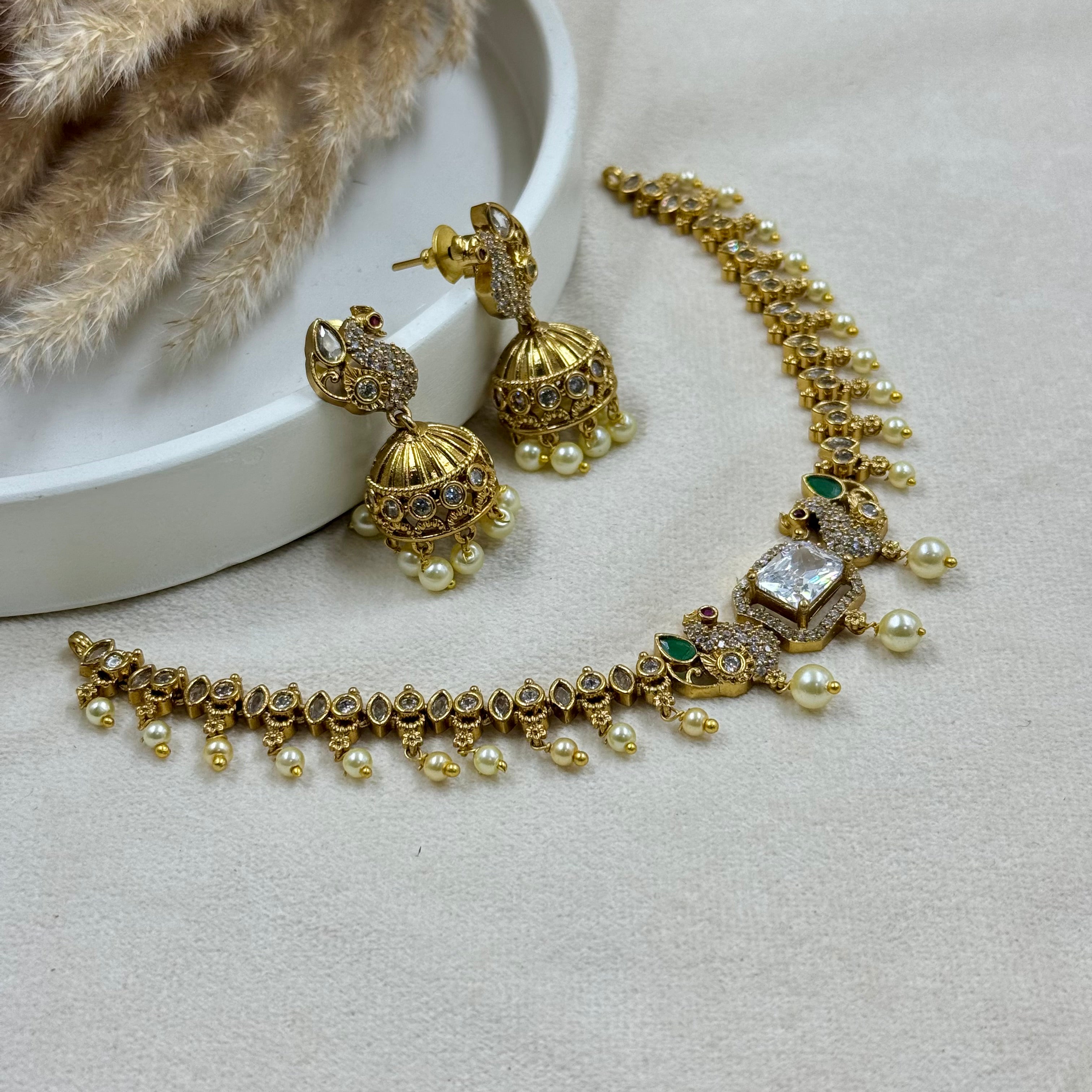 Gold necklace and earrings on a light gray surface with a white dish and beige fur.