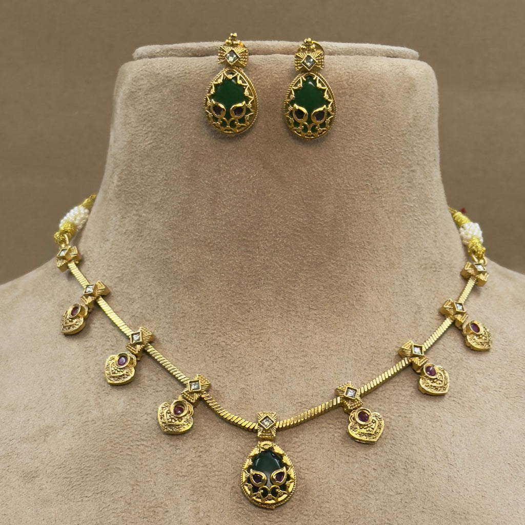 Gold necklace and earrings with green and purple stones on a mannequin bust.