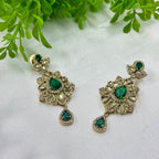 Pair of ornate earrings with green gemstones on a white background with green leaves.