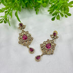 Ornate earrings with pink gemstones on a white background with green leaves.