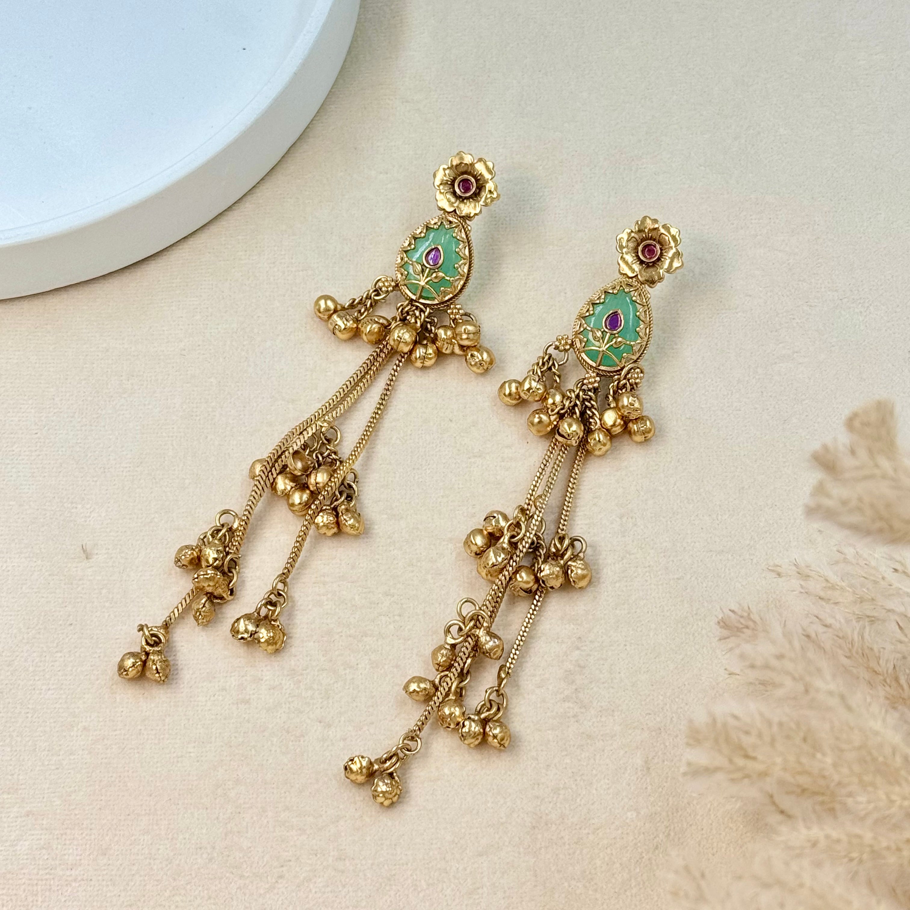 Gold earrings with green gemstones on a textured surface