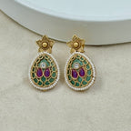 Pair of decorative earrings with gold, purple, and green details on a beige surface.