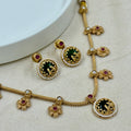 Gold necklace with green and red gemstones on a light background