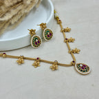 Gold necklace and earrings with gemstones on a light gray surface.