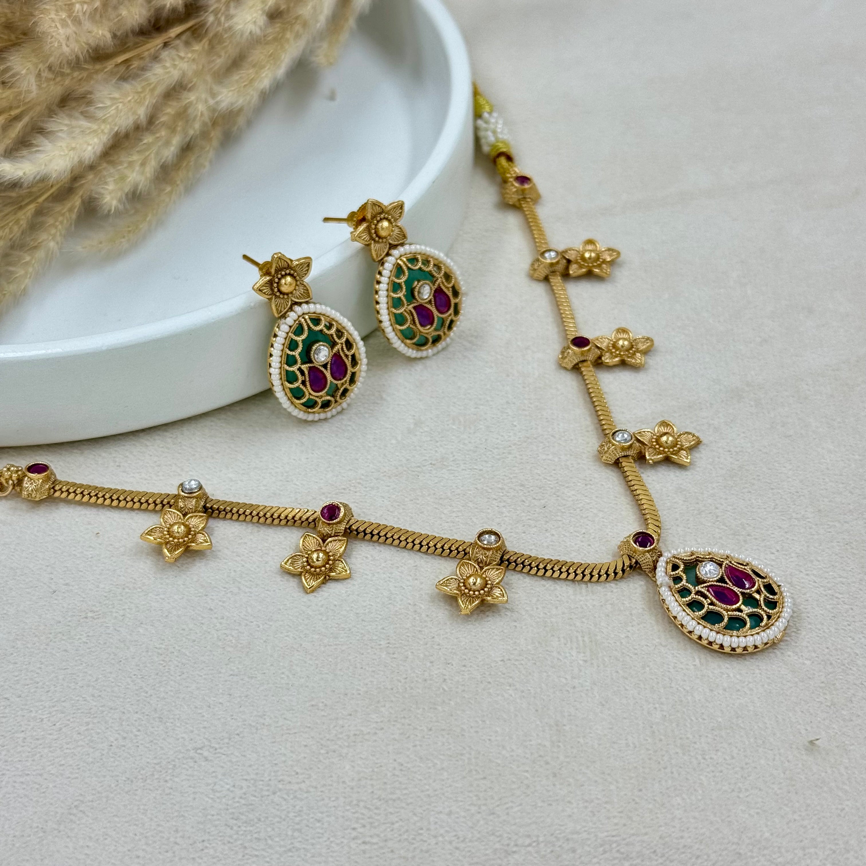 Gold necklace and earrings with gemstones on a light gray surface.