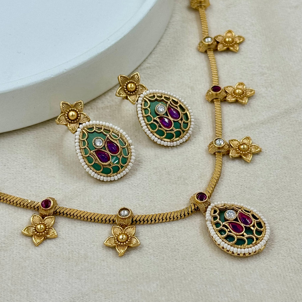 Gold necklace with green and red gemstones on a beige surface