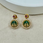 Gold earrings with green and red stones on a beige surface